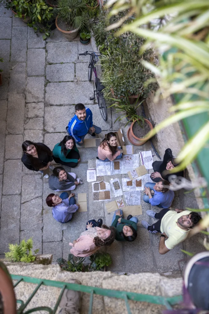 Workshop sCARTA in un cortile in pietra in Sardegna Vista dall'alto di un gruppo di persone sedute attorno a un tavolo di lavoro
